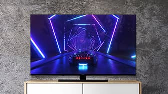 Fernseher von vorn, auf dem ein futuristisches Auto in einem neonbeleuchteten Tunnel mit sechseckigen Mustern auf einem strukturierten Wandhintergrund zu sehen ist.