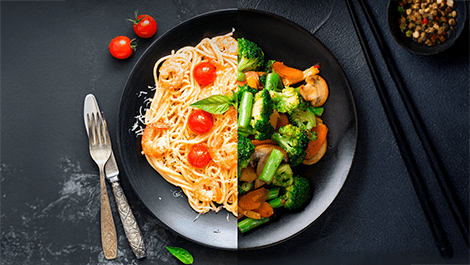 Ein Teller, aufgeteilt in eine Hälfte mit Garnelennudeln mit Tomaten und Basilikum und auf der anderen Seite mit gebratenem Gemüse mit Brokkoli und Karotten.