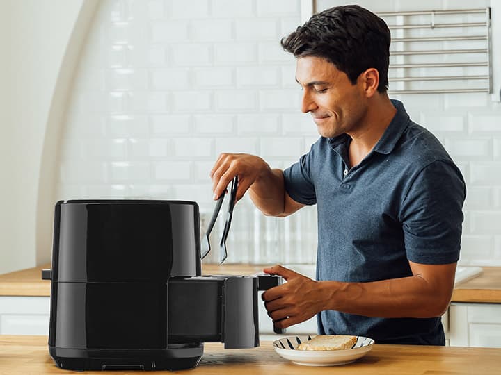 Ein Mann legt mit einer Zange Lebensmittel in eine schwarze Heißluftfritteuse in einer modernen Küche.