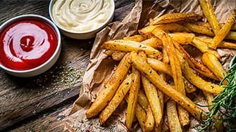 Knusprige Pommes mit Ketchup und Mayonnaise auf Backpapier – frisch zubereitet in der MEDION Heißluftfritteuse.