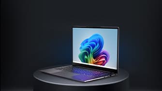 Aufgeklapptes von Rechts zu sehendes Laptop auf einem runden grauen Podest. Auf dem Display ist ein regenbogenfarbenes Muster zu sehen.