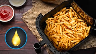 Goldene Pommes Frites im Korb einer Heißluftfritteuse auf einem Holztisch, daneben Ketchup und Mayonnaise in kleinen Schälchen. Ein Öltropfen-Symbol ist sichtbar.