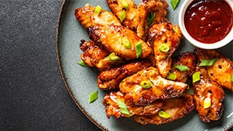 Knusprige Hähnchenflügel mit Glasur und Frühlingszwiebeln auf Teller – zubereitet in der MEDION Heißluftfritteuse.