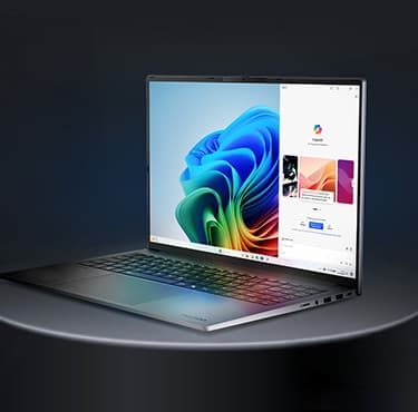 Ein schräg nach rechts gedrehter aufgeklappter Laptop auf einem grauen Hintergrund. Das Display zeigt einen Copilot Screen.