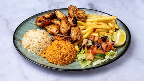 Ein Teller mit gegrilltem Hähnchen, Pommes frites, weißem und orangefarbenem Reis, frischem Salat und einer Zitronenscheibe auf einer Marmoroberfläche.