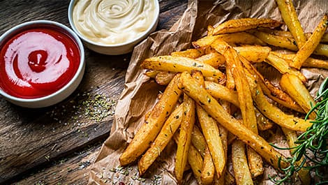 Knusprige Pommes mit Ketchup und Mayonnaise auf Backpapier – frisch zubereitet in der MEDION Heißluftfritteuse.