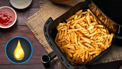 Goldene Pommes Frites im Korb einer Heißluftfritteuse auf einem Holztisch, daneben Ketchup und Mayonnaise in kleinen Schälchen. Ein Öltropfen-Symbol ist sichtbar.