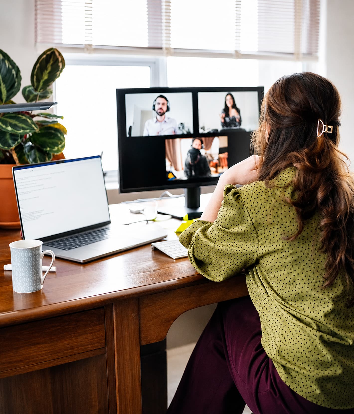 Person im Homeoffice bei einer Videokonferenz an einem Arbeitsplatz mit Monitor und Laptop