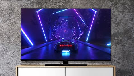 Fernseher von vorn, auf dem ein futuristisches Auto in einem neonbeleuchteten Tunnel mit sechseckigen Mustern auf einem strukturierten Wandhintergrund zu sehen ist.
