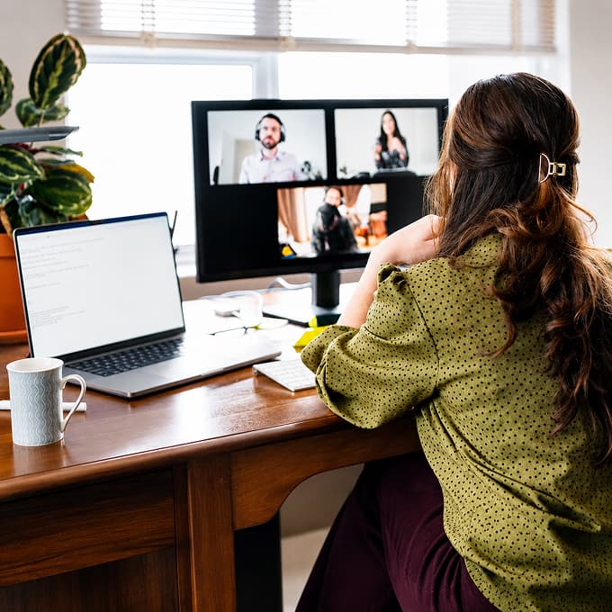 Person im Homeoffice bei einer Videokonferenz an einem Arbeitsplatz mit Monitor und Laptop