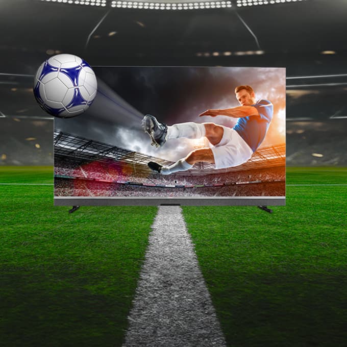 Fernseher auf Fußballfeld zeigt einen Spieler beim Schuss auf das Tor, Fußball fliegt aus dem Bildschirm heraus.