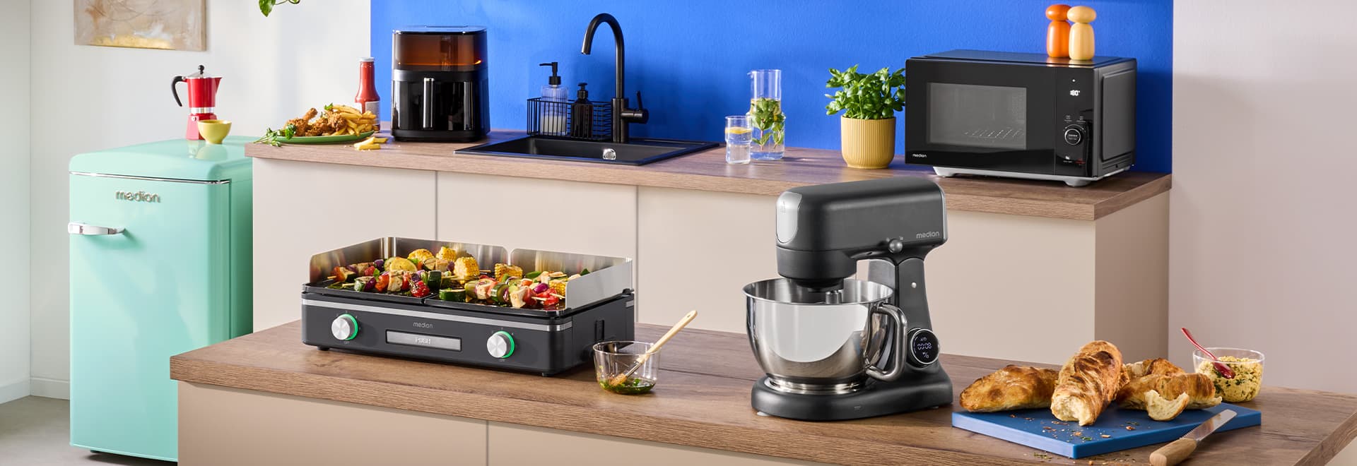 Moderne Küche mit einem Tischgrill, Mikrowelle, Küchenmaschine, Heißluftfritteuse und einem mint farbenen Kühlschrank.