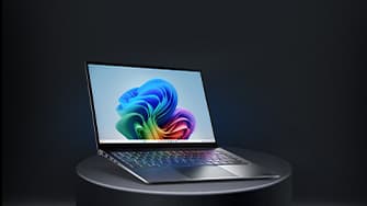 Aufgeklapptes von schräg vorne zu sehendes Laptop auf einem runden grauen Podest. Auf dem Display ist ein regenbogenfarbenes Muster zu sehen.