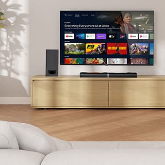 MEDION Fernseher auf einem TV-Möbel mit Soundbar und Subwoofer, dargestellt mit Smart-TV-Benutzeroberfläche und verschiedenen Streaming-Apps auf dem Bildschirm.