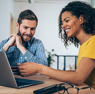 Zwei Personen sitzen gemeinsam vor einem MEDION Laptop in einem hellen Raum und lächeln.
