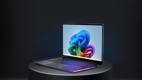 Aufgeklapptes von Rechts zu sehendes Laptop auf einem runden grauen Podest. Auf dem Display ist ein regenbogenfarbenes Muster zu sehen.