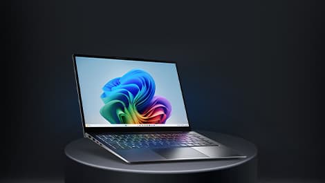 Aufgeklapptes von schräg vorne zu sehendes Laptop auf einem runden grauen Podest. Auf dem Display ist ein regenbogenfarbenes Muster zu sehen.