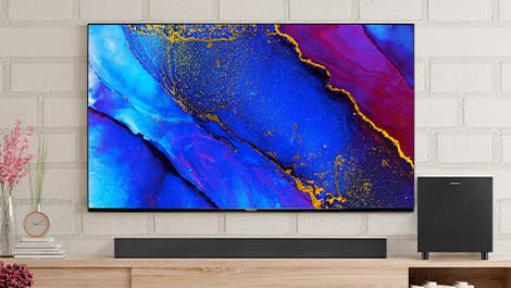 Ein Flachbildfernseher mit lebendiger abstrakter Kunst in Blau-, Rot- und Gelbtönen, der an einer Ziegelwand über einer Holzkonsole angebracht ist.