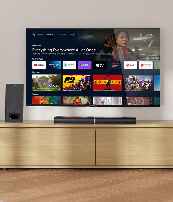 MEDION Fernseher auf einem TV-Möbel mit Soundbar und Subwoofer, dargestellt mit Smart-TV-Benutzeroberfläche und verschiedenen Streaming-Apps auf dem Bildschirm.