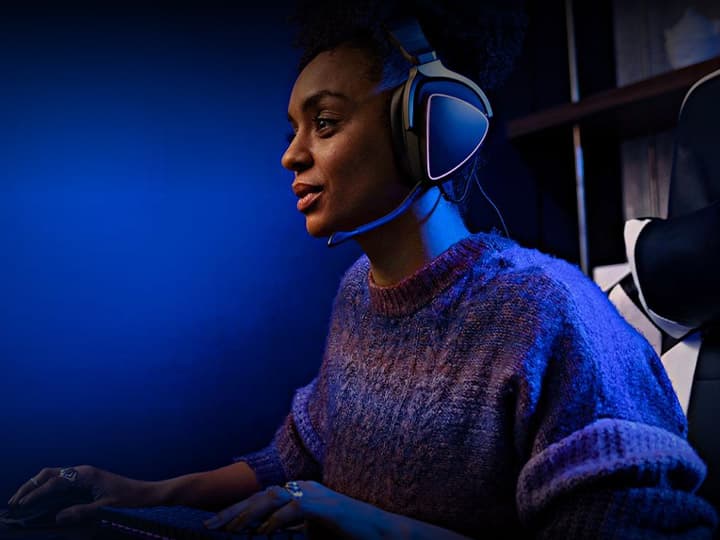 Eine Person mit Headset sitzt in einem schwach beleuchteten Raum mit blauer Beleuchtung und konzentriert sich auf einen Bildschirm.