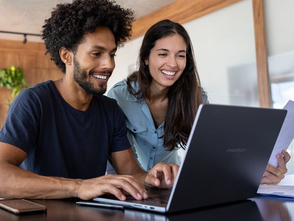 Mann und Frau sitzen lächelnd vor einem geöffneten Laptop in einem Büro